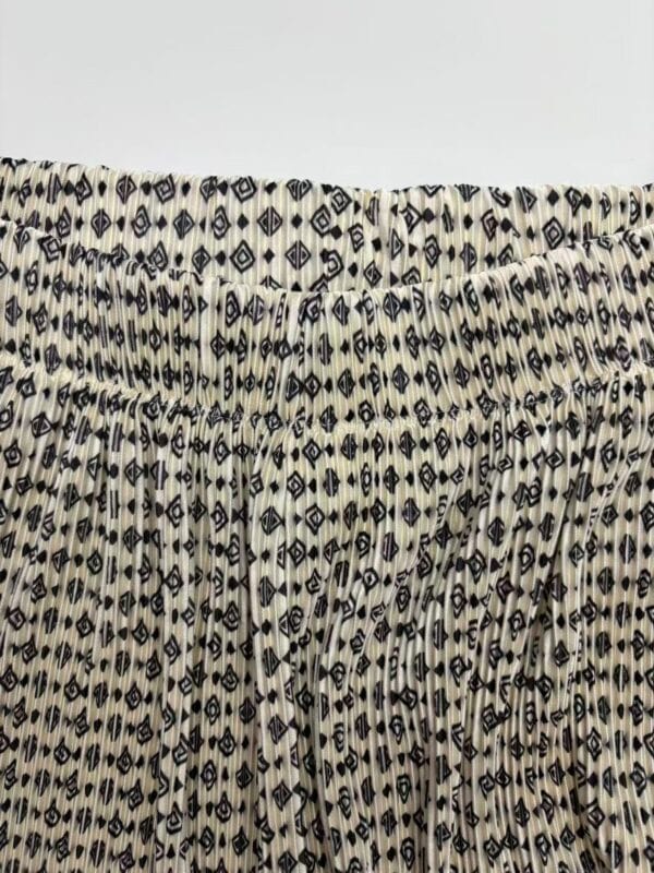 Close-up of fabric featuring a black and white geometric pattern with small diamond and square shapes, gathered at the top.