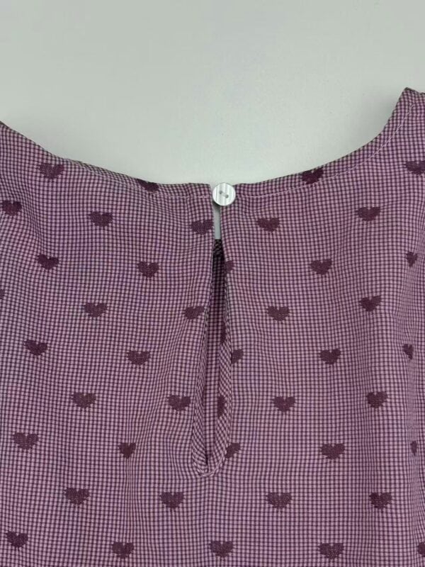 Close-up of pink checkered dress with small dark heart patterns and a zipper at the back for a stylish look.