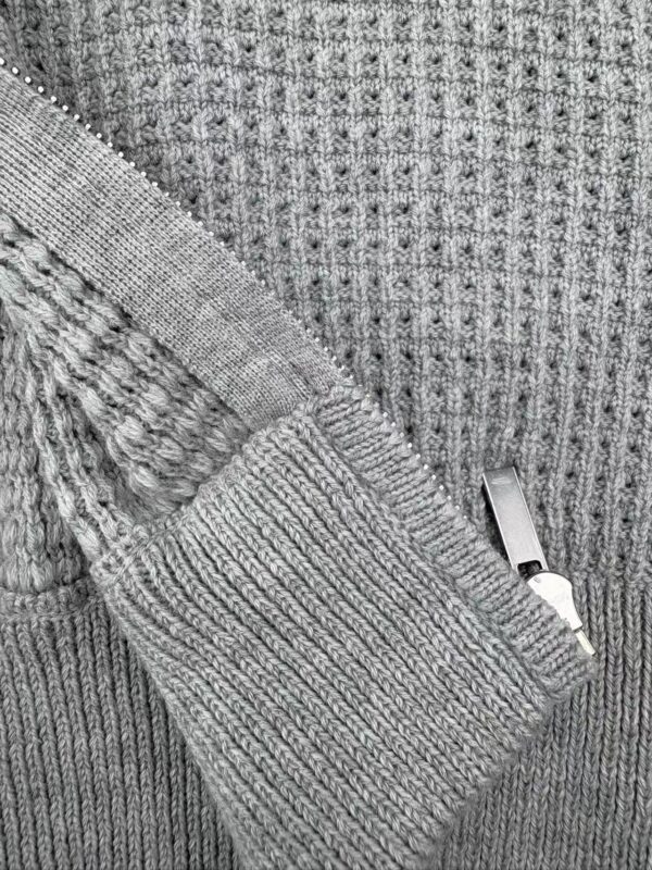 Close-up of a gray knit sweater featuring textured patterns and a silver zipper detail, showcasing cozy winter fashion for men and women.