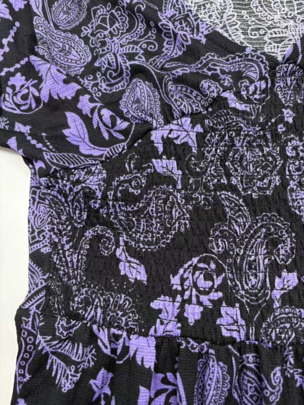 Close-up of a black dress with purple floral and paisley patterns, featuring an elastic waistband and intricate design details.