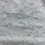 Close-up of intricate white lace fabric with floral and leaf patterns, ideal for wedding dresses and elegant fashion designs.
