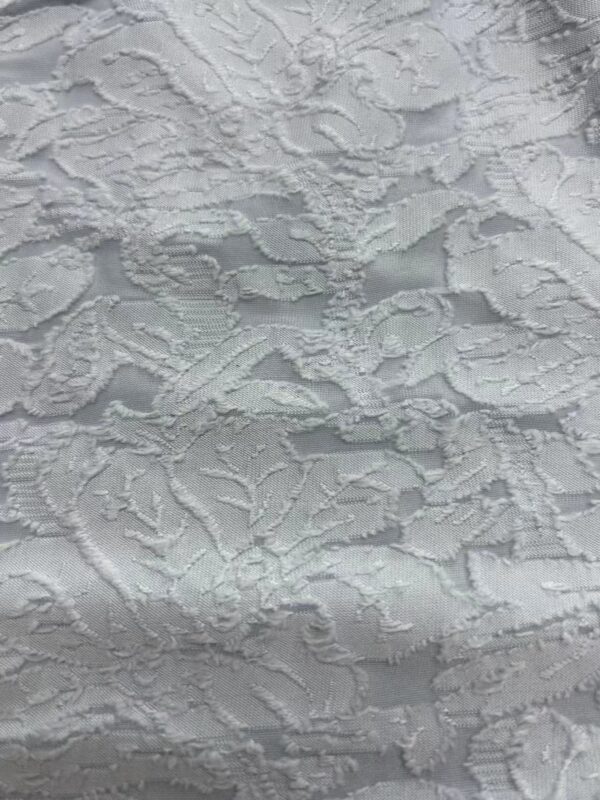 Close-up of intricate white lace fabric with floral and leaf patterns, ideal for wedding dresses and elegant fashion designs.