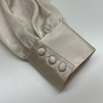 Close-up of a cream satin blouse sleeve with three fabric-covered buttons, showcasing luxurious fabric and detailed craftsmanship.