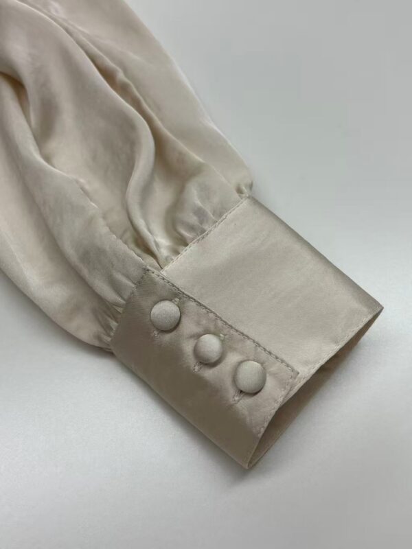 Close-up of a cream satin blouse sleeve with three fabric-covered buttons, showcasing luxurious fabric and detailed craftsmanship.