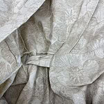 Close-up of light beige fabric with subtle floral and leaf patterns, gathered and draped to showcase texture and intricate design details.