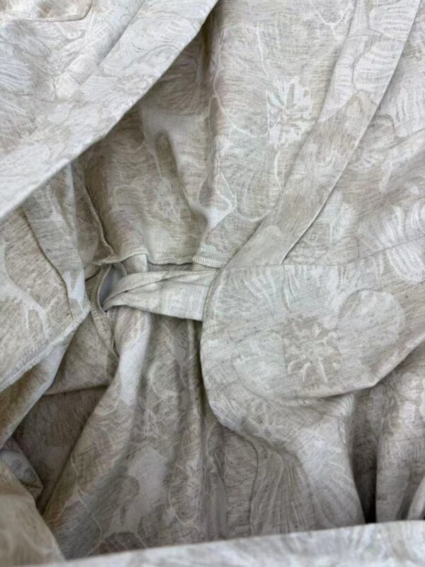 Close-up of light beige fabric with subtle floral and leaf patterns, gathered and draped to showcase texture and intricate design details.