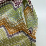 Close-up of vibrant zigzag patterned knit fabric with multicolor threads in shades of yellow, orange, purple, and green, showcasing detailed texture and craftsmanship.