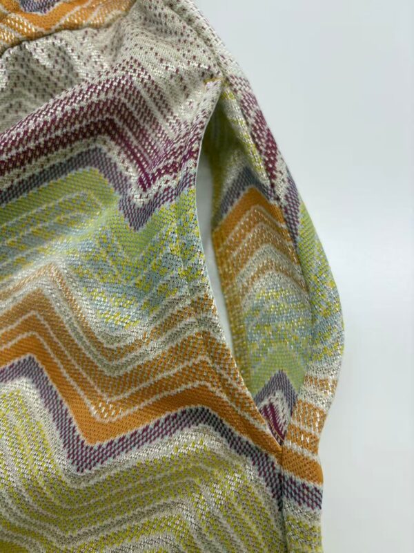Close-up of vibrant zigzag patterned knit fabric with multicolor threads in shades of yellow, orange, purple, and green, showcasing detailed texture and craftsmanship.