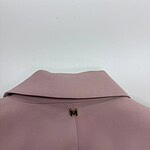 Close-up of a soft pink blouse featuring a folded collar and a small gold 'M' embellishment at the neckline, perfect for stylish casual or office wear.