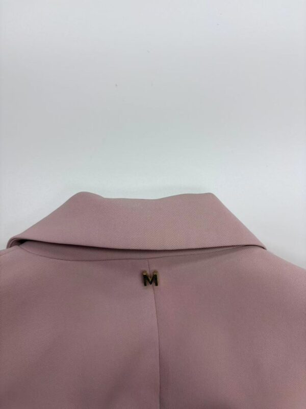 Close-up of a soft pink blouse featuring a folded collar and a small gold 'M' embellishment at the neckline, perfect for stylish casual or office wear.