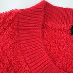 Close-up of a vibrant red knit sweater with textured fabric and ribbed collar, perfect for fall and winter fashion.
