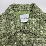 Close-up of a green tweed women's jacket with a collar and button closure, showcasing textured fabric and stylish design.