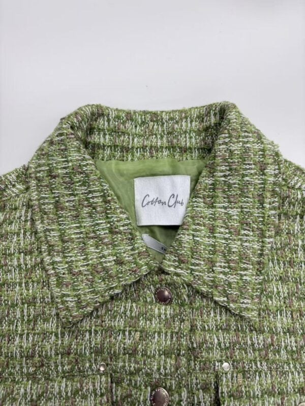Close-up of a green tweed women's jacket with a collar and button closure, showcasing textured fabric and stylish design.