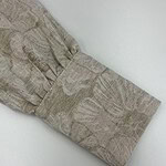 Close-up of a fabric cuff with a subtle leaf pattern in neutral tones, showcasing fine stitching and craftsmanship.