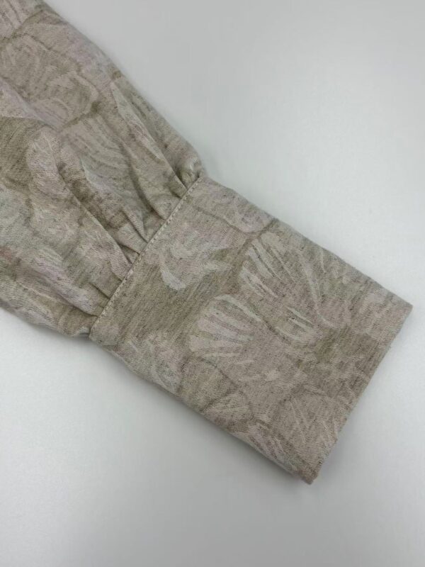 Close-up of a fabric cuff with a subtle leaf pattern in neutral tones, showcasing fine stitching and craftsmanship.