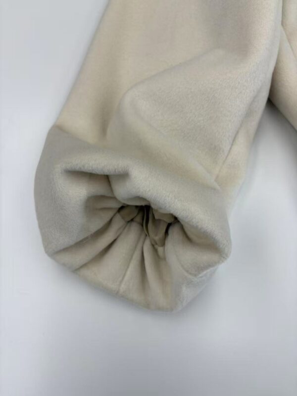 Close-up of a cream-colored fabric sleeve with gathered elastic cuff, showcasing soft texture and elegant design for fashion and clothing.