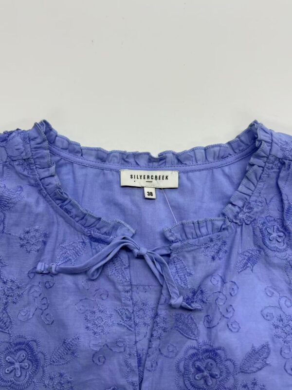 Close-up of a blue embroidered blouse with ruffled neckline and tie detail, perfect for stylish casual or semi-formal wear.