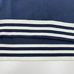 Close-up of navy blue fabric with white and navy striped ribbed trim, showcasing textile detail and pattern.