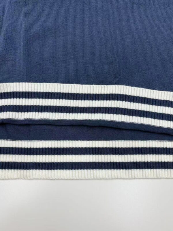 Close-up of navy blue fabric with white and navy striped ribbed trim, showcasing textile detail and pattern.