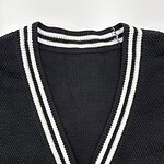 Close-up of a black V-neck cardigan with white striped trim, made of textured knit fabric, featuring a small pocket on the front.