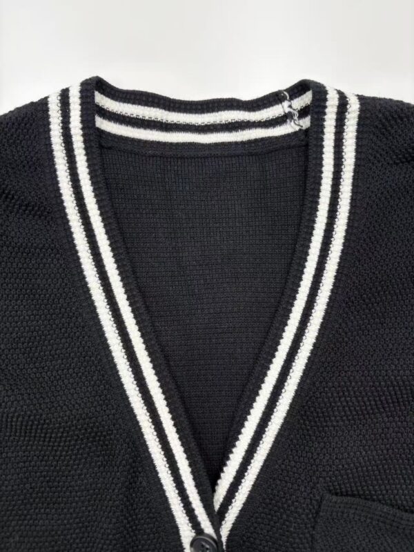 Close-up of a black V-neck cardigan with white striped trim, made of textured knit fabric, featuring a small pocket on the front.