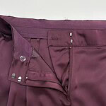 Close-up of burgundy women's dress pants showing zipper, button, and waistband details for formal wear.