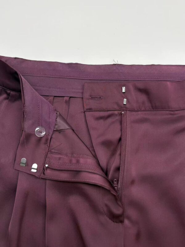 Close-up of burgundy women's dress pants showing zipper, button, and waistband details for formal wear.