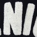 Detailed view of white embroidered letters on black fabric, highlighting texture and stitching quality.
