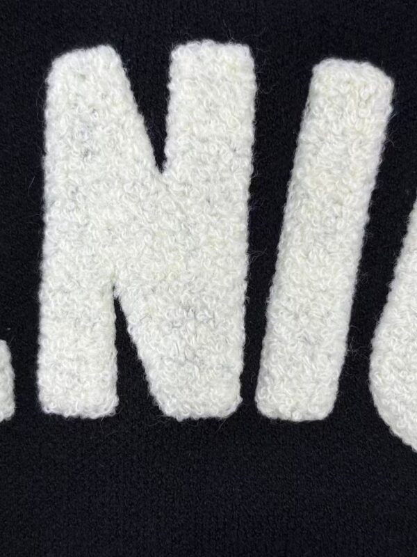 Detailed view of white embroidered letters on black fabric, highlighting texture and stitching quality.