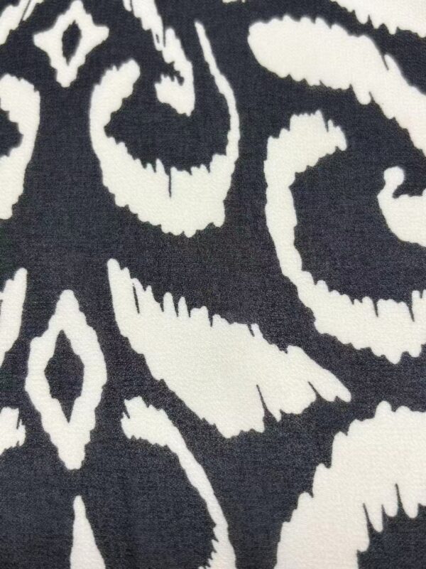 Close-up of a black and white patterned fabric with intricate swirling and geometric designs, ideal for fashion and home decor.