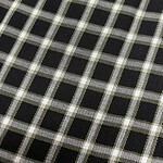 Close-up of black fabric with a white and green checkered pattern, showcasing detailed textile design for fashion or upholstery use.