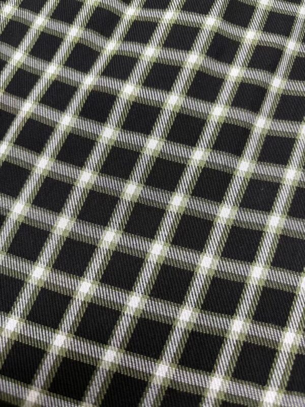 Close-up of black fabric with a white and green checkered pattern, showcasing detailed textile design for fashion or upholstery use.