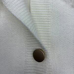 Close-up of a white knit cardigan featuring two gold buttons, showcasing soft fabric and fine craftsmanship, ideal for fashion and clothing accessories.