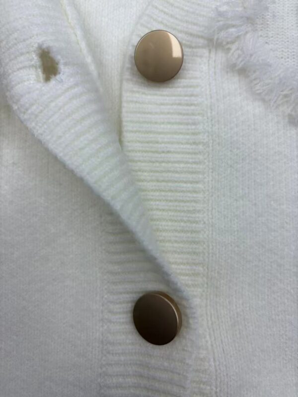 Close-up of a white knit cardigan featuring two gold buttons, showcasing soft fabric and fine craftsmanship, ideal for fashion and clothing accessories.
