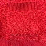 Close-up of a red textured sweater featuring a ribbed pocket detail, perfect for winter fashion and casual wear.