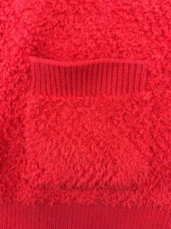 Close-up of a red textured sweater featuring a ribbed pocket detail, perfect for winter fashion and casual wear.
