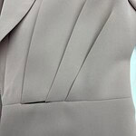 Close-up of a light gray suit fabric with tailored pleats and smooth texture, showcasing high-quality material and craftsmanship.