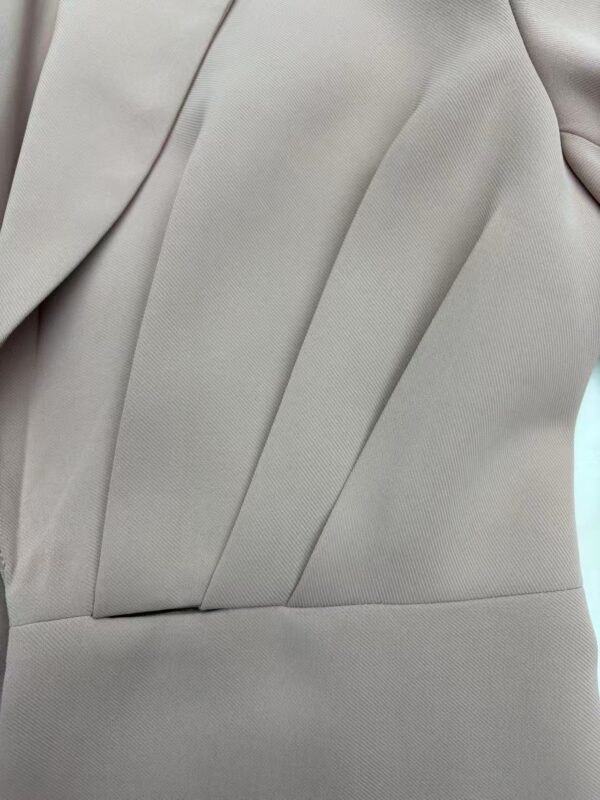 Close-up of a light gray suit fabric with tailored pleats and smooth texture, showcasing high-quality material and craftsmanship.