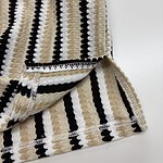 Close-up of beige, black, and white striped knitted fabric, showcasing texture and pattern suitable for clothing or accessories.