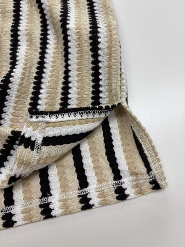 Close-up of beige, black, and white striped knitted fabric, showcasing texture and pattern suitable for clothing or accessories.