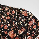 Close-up of black fabric with vibrant red, pink, and beige floral print, showcasing detailed design and texture for fashion or textile use.