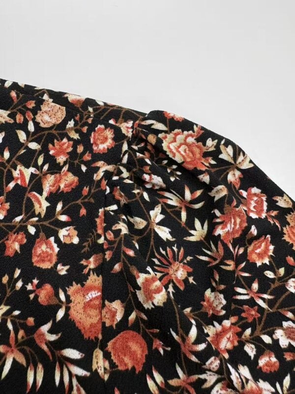Close-up of black fabric with vibrant red, pink, and beige floral print, showcasing detailed design and texture for fashion or textile use.