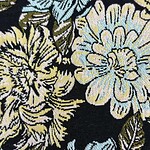 Close-up of floral patterned fabric featuring large yellow, blue, and green flowers on a black background, ideal for fashion and textile projects.