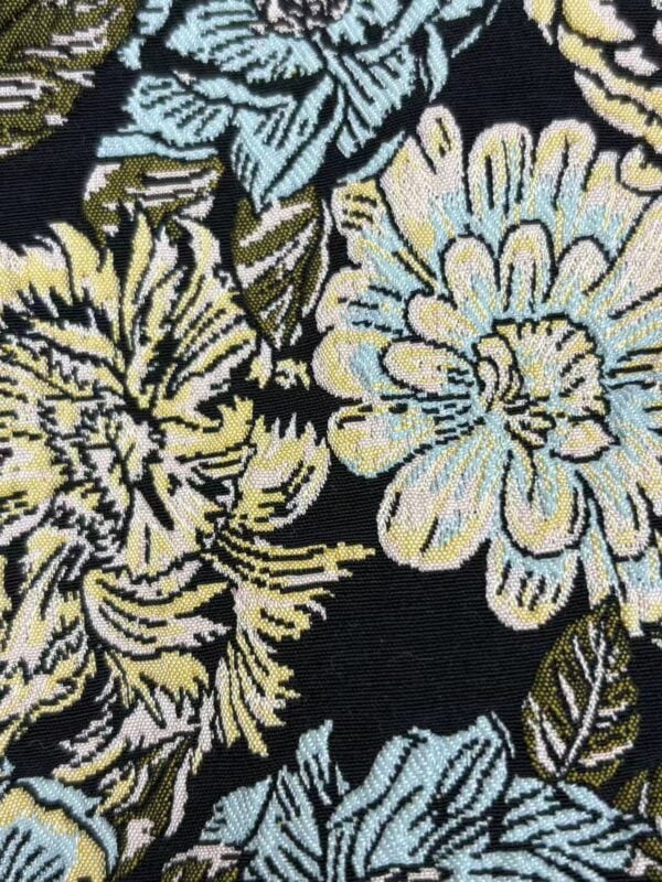 Close-up of floral patterned fabric featuring large yellow, blue, and green flowers on a black background, ideal for fashion and textile projects.