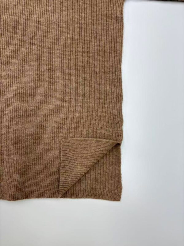Close-up of a brown ribbed sweater fabric with a folded corner, showcasing its texture and warm tone.
