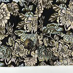 Close-up of fabric with floral pattern in beige, blue, and green on black background, featuring buttons.