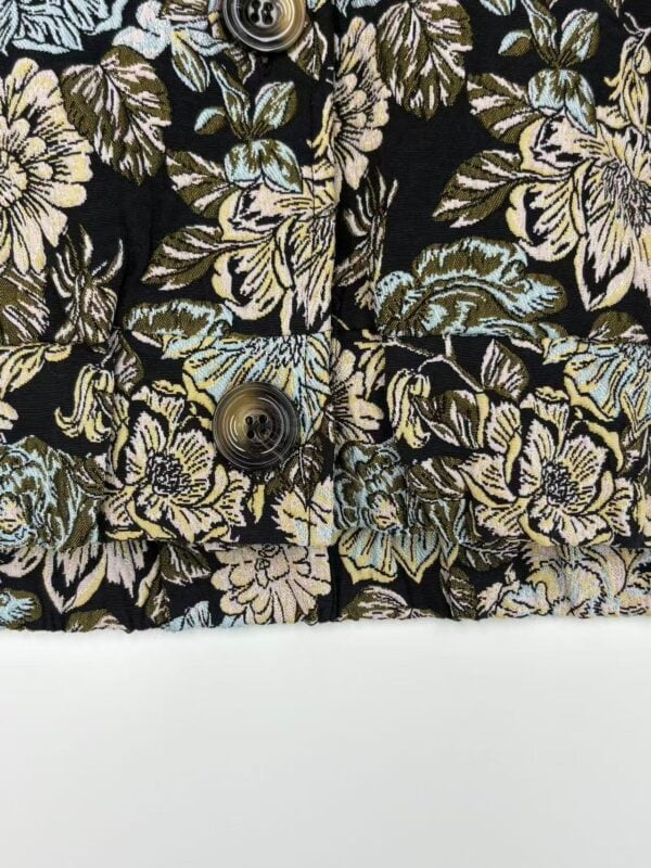 Close-up of fabric with floral pattern in beige, blue, and green on black background, featuring buttons.