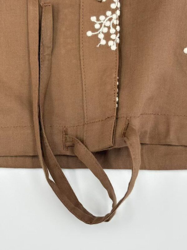 Close-up of brown fabric with white embroidered floral pattern and tied fabric straps, suitable for fashion or textile product SEO.