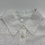 Close-up of a white embroidered women's shirt with eyelet floral patterns and a classic collar, perfect for casual or formal wear.