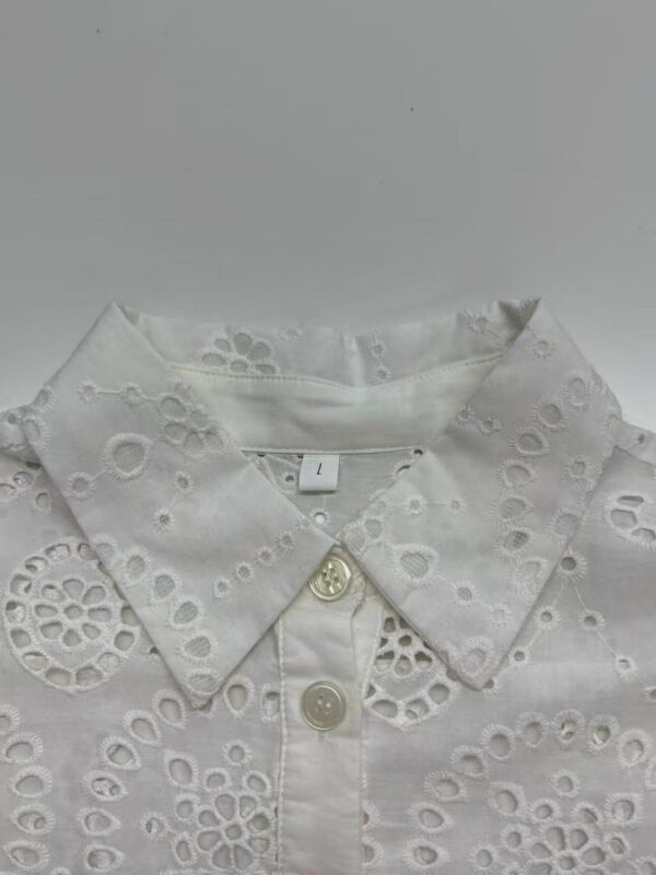Close-up of a white embroidered women's shirt with eyelet floral patterns and a classic collar, perfect for casual or formal wear.